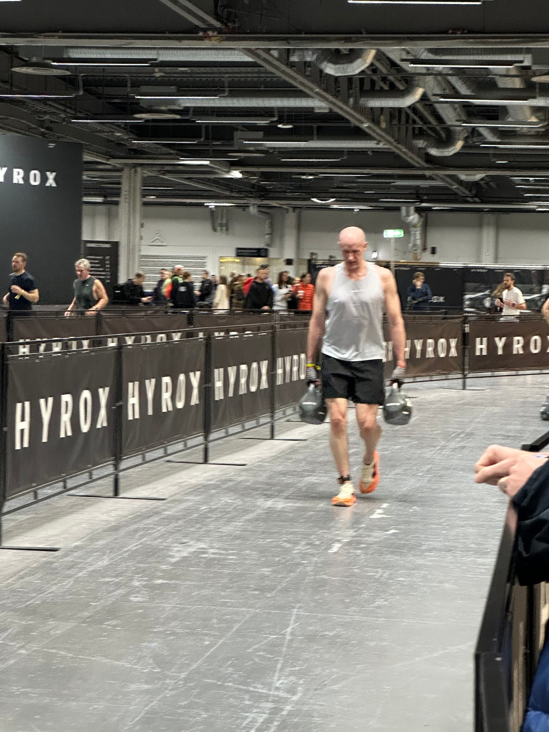 Age-group HYROX athlete carrying kettlebells during a race